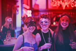 three women wearing fancy dress smiling and drinking champagne