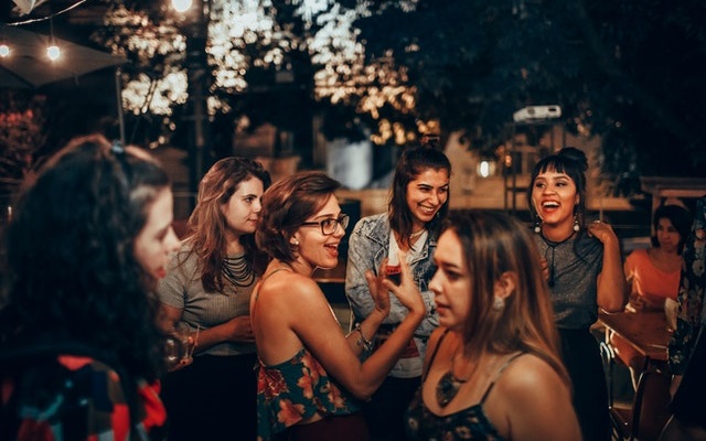 Group of 6 women chatting and having drinks at a party outdoors